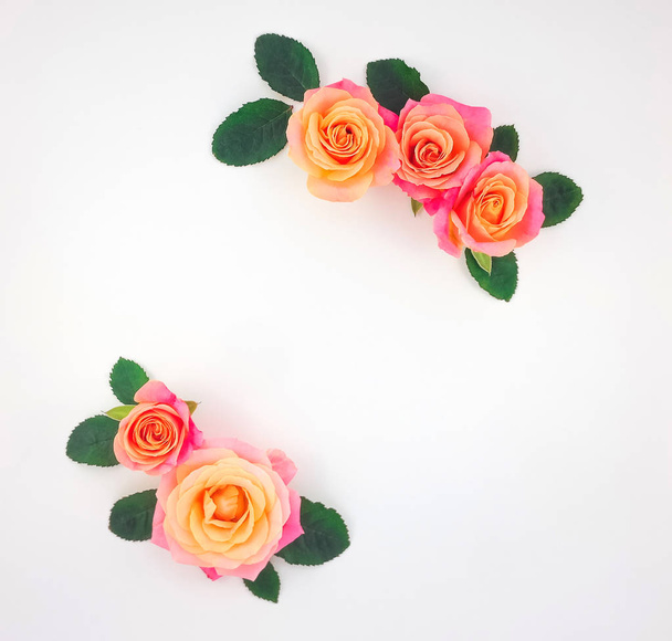 Frame made of pink-orange roses and green leaves on white background. Flat lay, top view - Foto, afbeelding