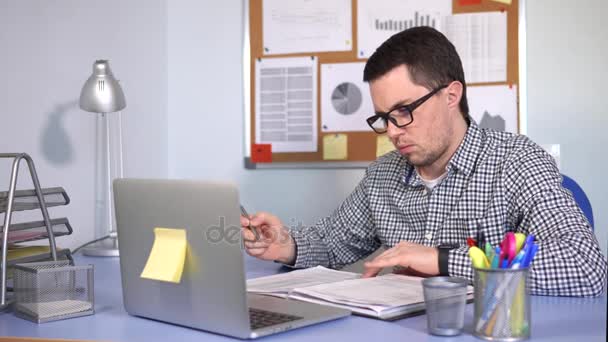 Διευθυντής συμπληρώνει έντυπα στο χώρο εργασίας και εξετάζει την οθόνη του φορητού υπολογιστή - Πλάνα, βίντεο