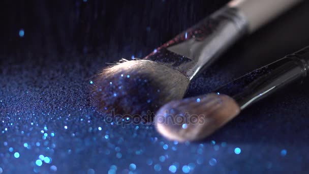 Blue shiny sparkles falling on makeup brushes on the black background, abstract slow motion - Video