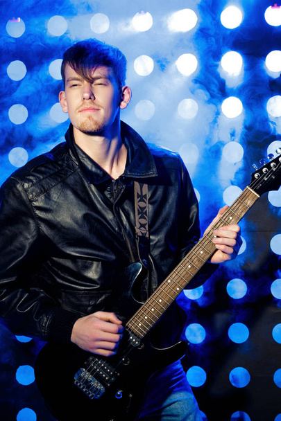 young attractive rock musician playing electric guitar and singing. Rock star on background of spotlights - Foto, imagen
