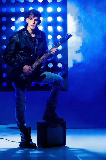 young attractive rock musician playing electric guitar and singing. Rock star on background of spotlights - Foto, Imagen