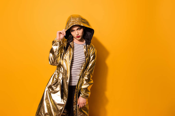 Fashionable girl is in shining gold coat with a hood on the yell - Foto, Imagen