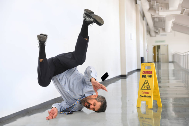 Senior businessman falling on wet floor inside office building - Фото, изображение