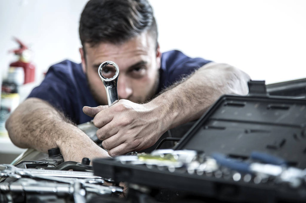 Car mechanic man at the garage fixing the engine - Фото, изображение