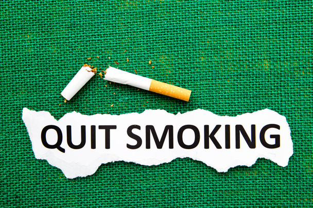 Quit Smoking - with broken cigarette and printed text on green burlap background - Photo, Image