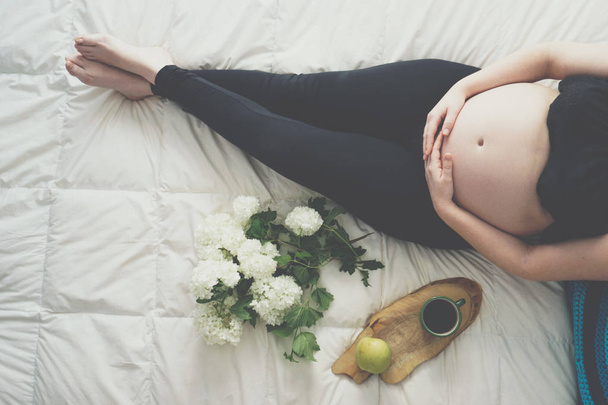 Donna incinta è sdraiata sul letto, vista dall'alto
 - Foto, immagini