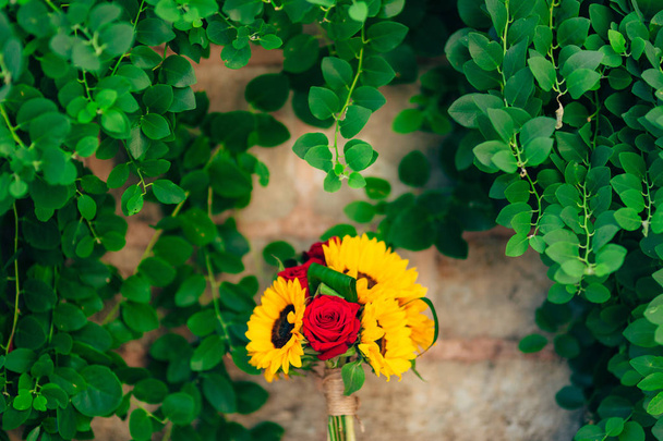 Häät morsiuskimppu auringonkukkia kivi penkki ja roikkuu taustalla vihreitä lehtiä. Häät Montenegrossa, Perast
. - Valokuva, kuva