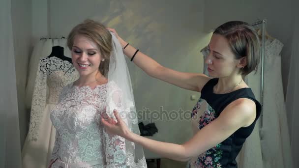 Braut im Kleidergeschäft für Hochzeitskleider wählt sie ein Kleid und der Designer unterstützt sie - Filmmaterial, Video
