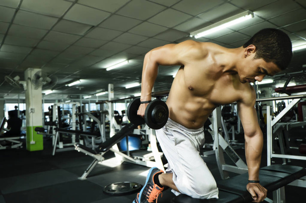 Fitness man in training, showing exercises with dumbbells in gym - 写真・画像