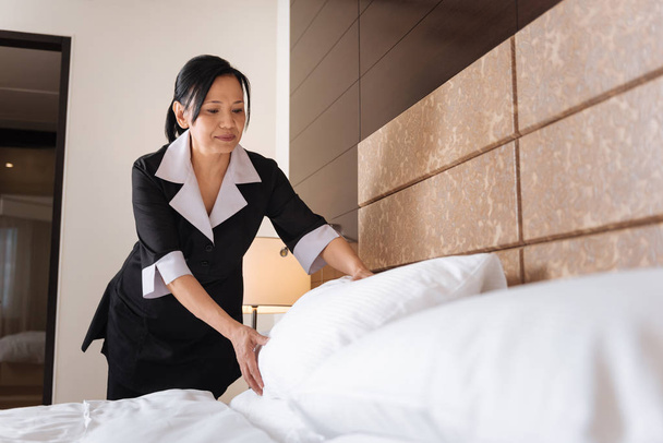 Pleasant delighted hotel maid making the bed - Fotó, kép
