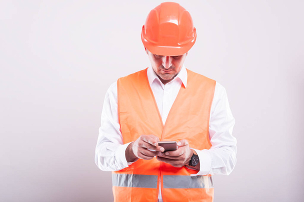 Εργοδηγός φορώντας αντανακλαστικό γιλέκο περιήγηση ή γραπτών μηνυμάτων στο smartphon - Φωτογραφία, εικόνα