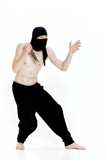 ninja man holds knife and is ready to attack on white background - 写真・画像