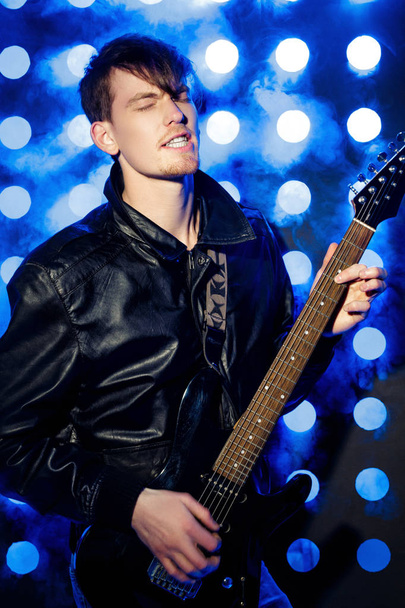 young attractive rock musician playing electric guitar and singing. Rock star on background of spotlights - Фото, зображення