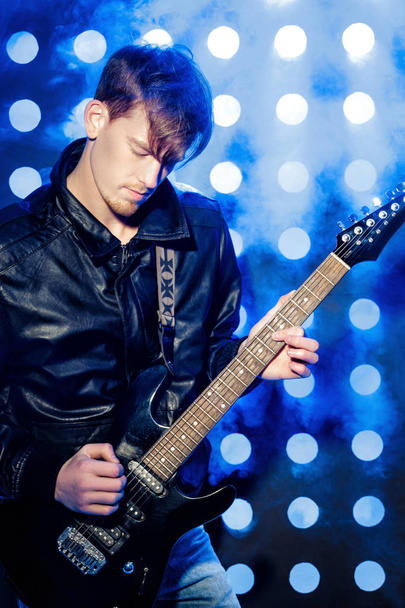 young attractive rock musician playing electric guitar and singing. Rock star on background of spotlights - Φωτογραφία, εικόνα