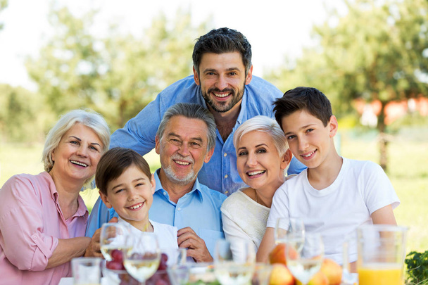Family sitting at table outdoors, smiling - Foto, Imagem
