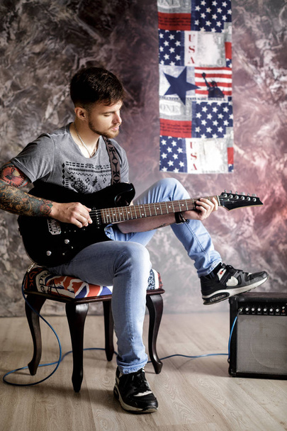 Young handsome musician playing electric guitar on dark background - 写真・画像