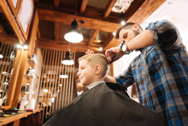 Experienced serious hairdresser combing the boys hair - Φωτογραφία, εικόνα