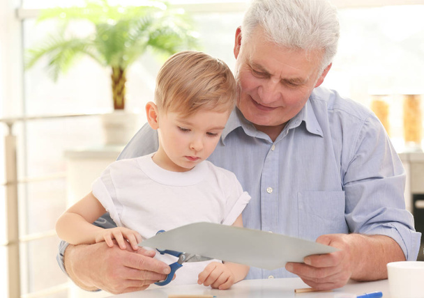 Senior man cutting paper together with grandson - Fotoğraf, Görsel