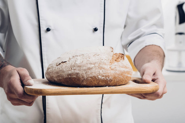 Fresh baked bread  on wooden board in  hands of  baker. soft light - Fotó, kép
