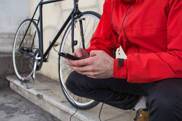 close up picture of cellphone in hands and black bicycle on background - Φωτογραφία, εικόνα