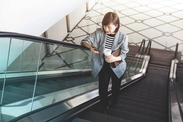 Mujer trabajadora usa teléfono inteligente mientras escaleras mecánicas
 - Foto, imagen