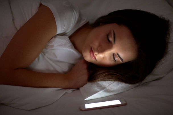 woman with smartphone sleeping in bed at night - Foto, imagen