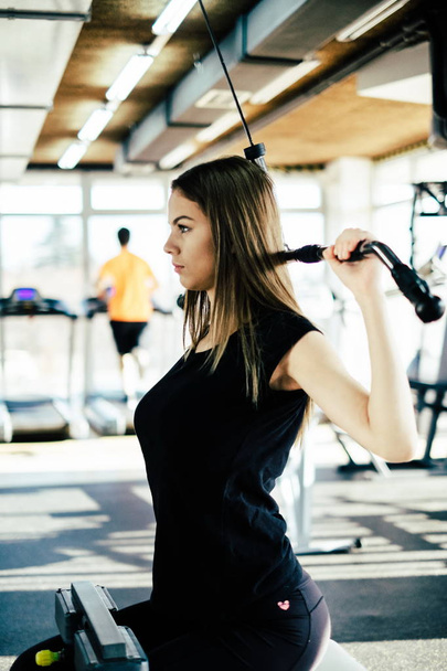 Young beautiful girl exercising in the fitness gym, with lat machine - Fotoğraf, Görsel