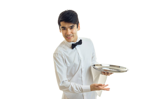 atractivo joven camarero en una camisa blanca sonriendo inclinado hacia adelante y sosteniendo una bandeja
 - Foto, imagen