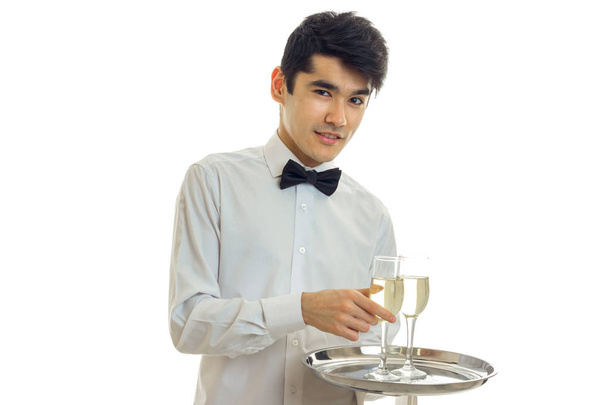 czarujący młody kelner uśmiechy, patrzy na aparat i taca z kieliszków szampana - Zdjęcie, obraz