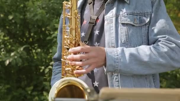Σαξόφωνο στα χέρια του μουσικούς του δρόμου στο τζιν σακάκι με συγχορδίες - Πλάνα, βίντεο