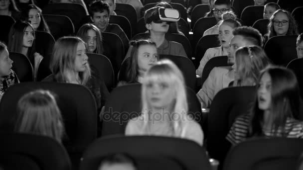 Маленькие дети подростки в кинотеатре смотрят на мальчика в очках виртуальной реальности. Черно-белые кадры
. - Кадры, видео