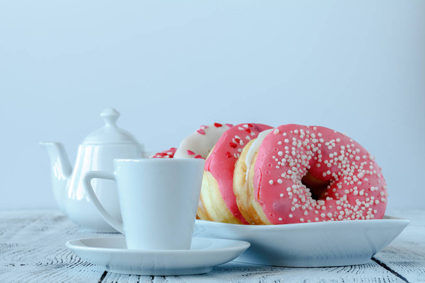Donuts with white icing and sprinkling on wooden board with cup of coffee - Valokuva, kuva