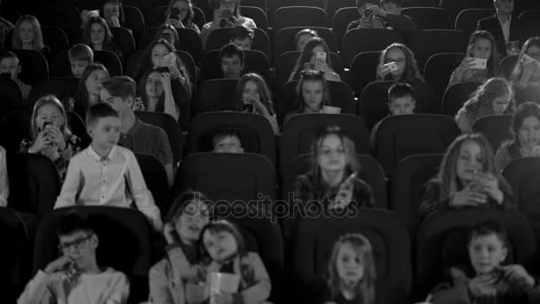 glückliche Kinder im Kino, die einen Cartoon gucken und Telefone aufblitzen lassen. Schwarz-Weiß-Aufnahme. - Filmmaterial, Video