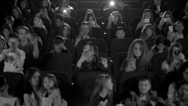 Des enfants heureux au cinéma regardant un dessin animé et faisant clignoter le téléphone. Plan noir et blanc
. - Séquence, vidéo