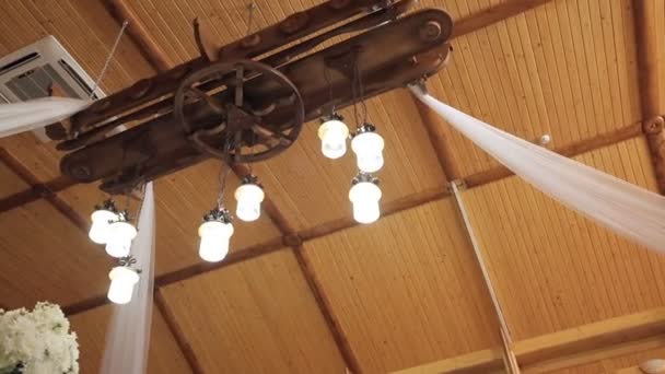 Rustikální lustr na vysokém stropě v dřevěném domě. Sál s květinami na oslavu - Záběry, video