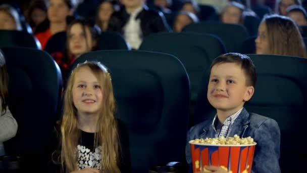 Kleine jongen en meisje eten popcorn, drinken van cola, glimlachen en kijken een film in de bioscoop met enthousiasme. - Video