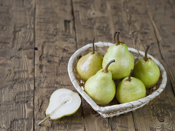 A cut pear and a basket with pears on a wooden table. - Photo, Image