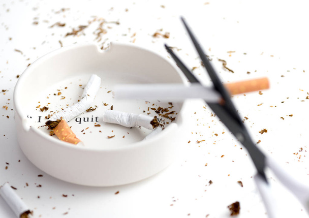 cenicero blanco con cigarrillo destruido y tijeras borrosas de hoja negra que cortan el cigarrillo como forground
 - Foto, Imagen