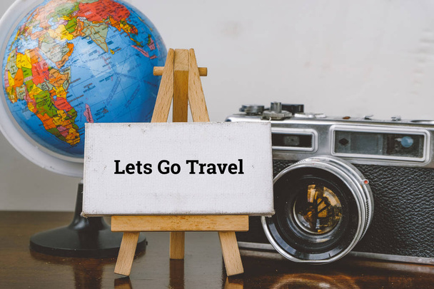 Utazás és nyaralás koncepció kép, szó Lets Go utazási és a festőállvány, a globe és a fából készült íróasztal vintage kamera elrendezés - Fotó, kép