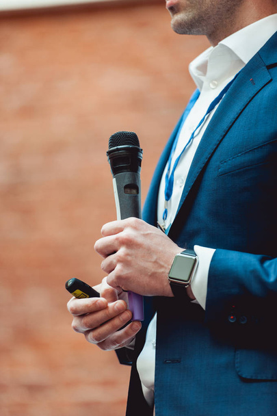İş ve konuşma konu: gri bir mikrofon tutan mavi elbiseli adam bir turuncu tuğla zemin üzerine - Fotoğraf, Görsel