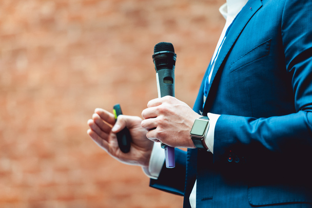 Business en spraak onderwerp: Man in een blauw pak houden een grijze microfoon een op een oranje bakstenen-achtergrond - Foto, afbeelding