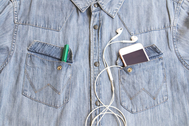 背景テクスチャ ジーンズ シャツ デニム生地とポケットにイヤホンと携帯電話 - 写真・画像