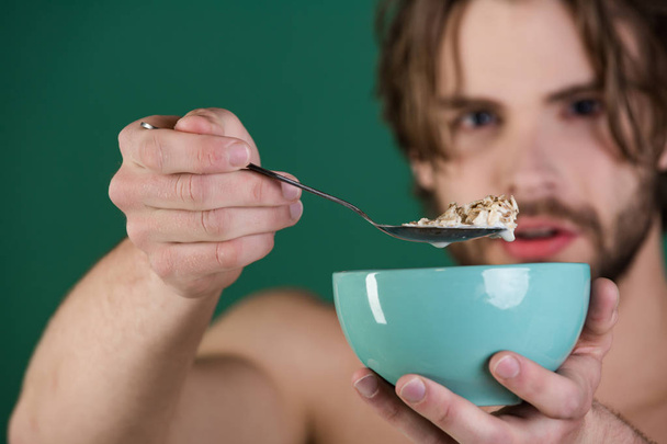 Сніданок. Красивий бородатий молодий чоловік має здоровий сніданок. Чоловік їсть сніданок з ложкою. Чоловік їсть зернові на сніданок. Красивий молодий чоловік має здоровий сніданок
 - Фото, зображення