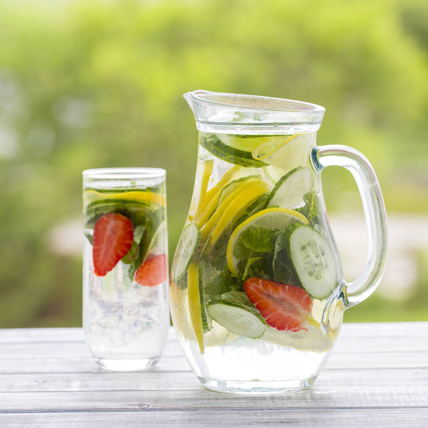 Dietary detox drink with lemon juice, red strawberry, cucumber and mint leaves in clear water with ice. - Фото, зображення