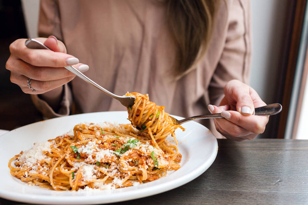girl eats Italian pasta with tomato, meat. Close-up spaghetti Bolognese wind it around a fork with a spoon. Parmesan cheese - Photo, Image