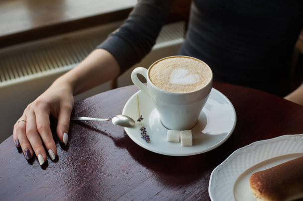 Kopje koffie met schuim en tiramisu taart op tafel - Foto, afbeelding
