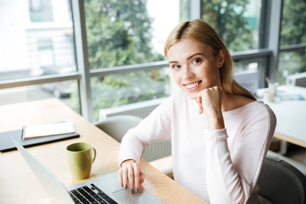 Cheerful lady sitting in office coworking while using laptop - Photo, Image