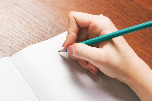 Closeup photo of girl writing in notebook with pencil - Foto, afbeelding