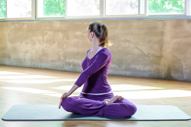 Mooie sportieve jonge vrouwelijke make yoga praktijk, de lotuspositie Padmasana draaien, uitrekken, pilates tijd met perfecte meisje. Volledig terugdraaien - Foto, afbeelding