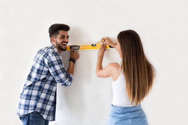 Smiling young couple measuring wall with level tool, renovation  - Foto, Imagen